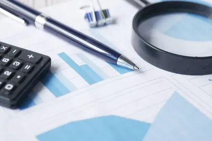 A magnifying glass, a pen, and a calculator on top of a document with blue bar charts